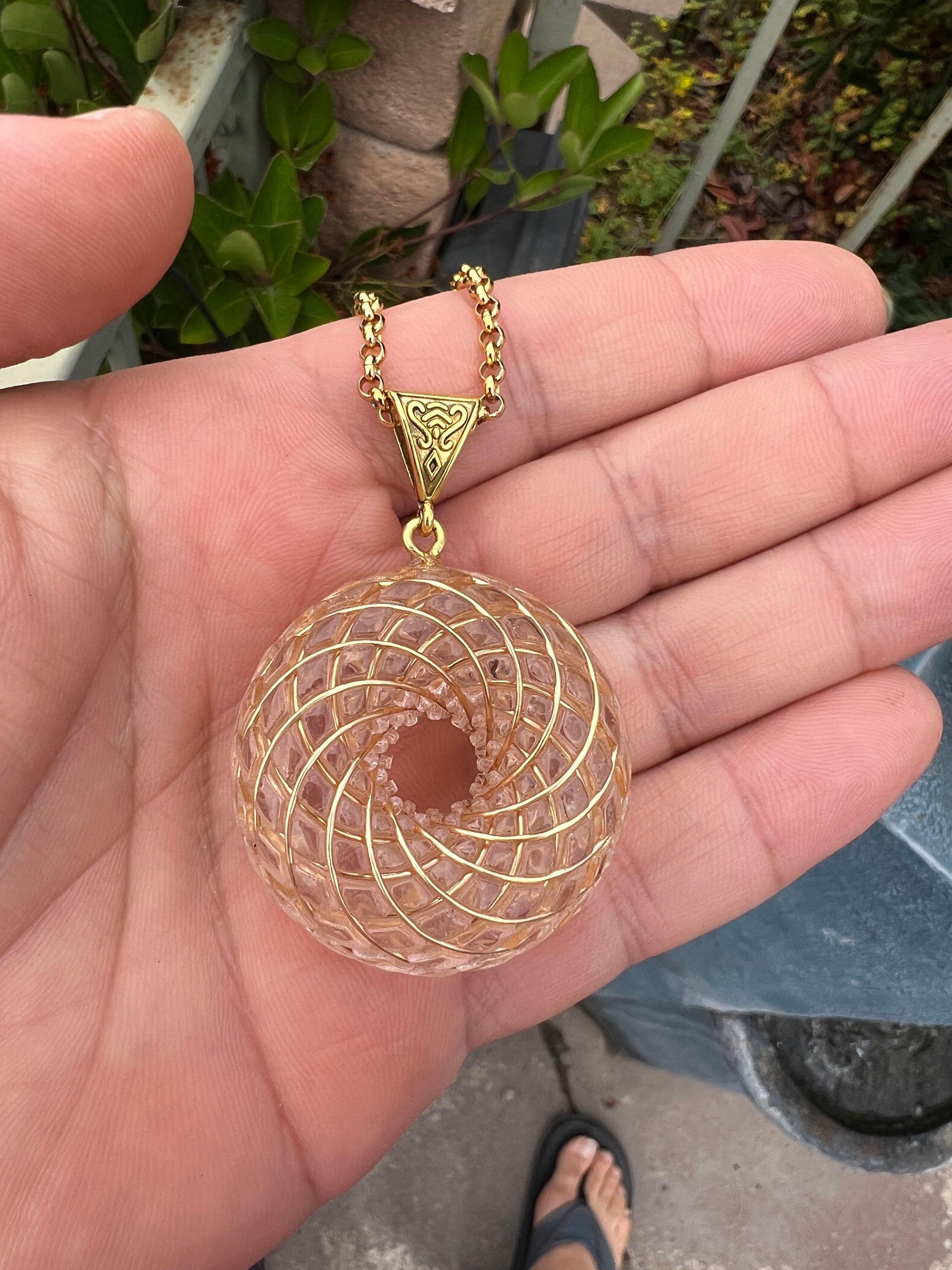 Hand holding Rainbow Phenakite crystal 18K pendant with gold chain and intricate spiral design